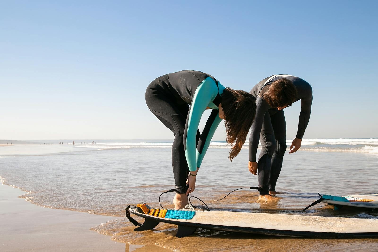 Two surfers attaching ankle leashes on a Moroccan beach in matching wetsuits