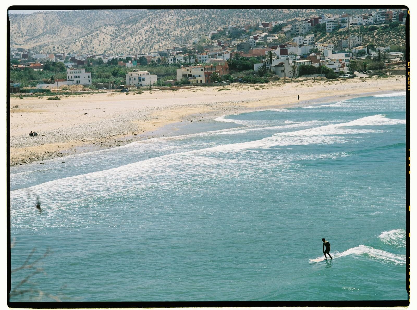 Aerial view of a Moroccan beach with a single surfer and mountain backdrop